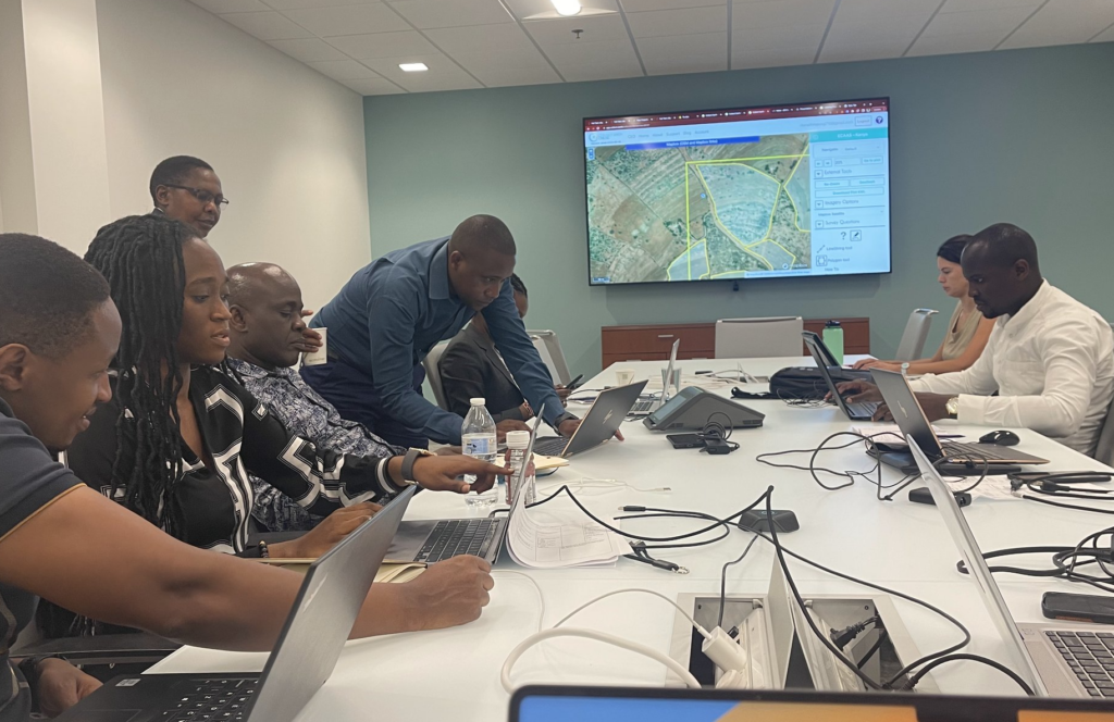 A group of people sit at a conference table using laptops to manipulate land mapping data.