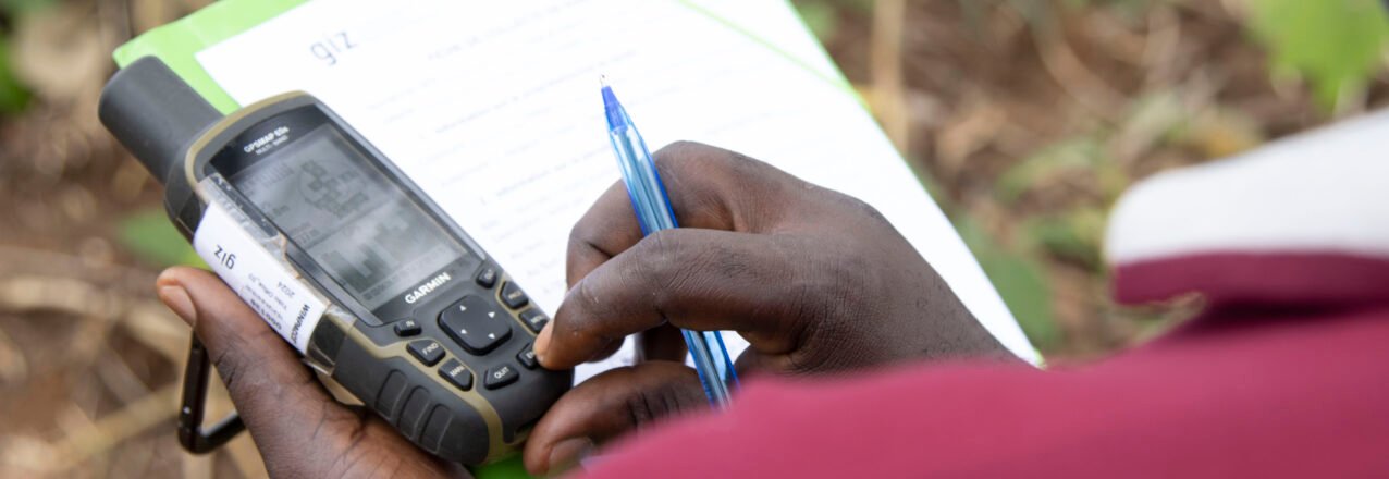 A person records land information on a clipboard while holding a GPS device in Cameroon.
