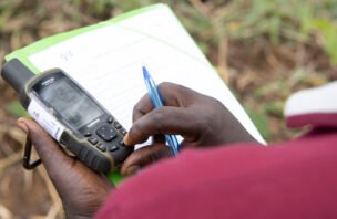 A person records land information on a clipboard while holding a GPS device in Cameroon.